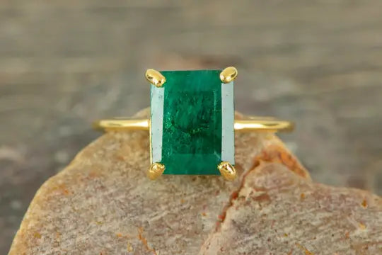 Emerald-cut green gemstone in a gold ring, a stunning natural emerald engagement ring.