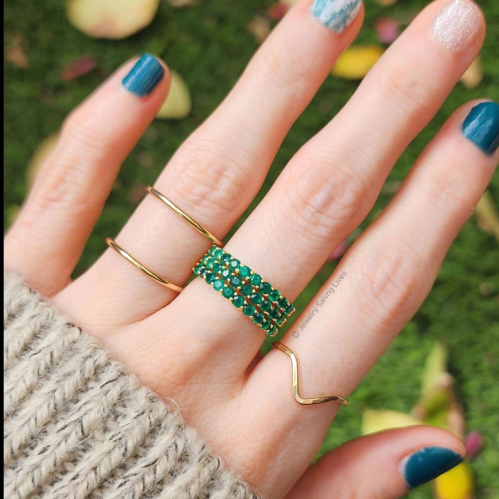 Hand adorned with gold rings and blue nail polish, showcasing an Emerald Half Eternity Band