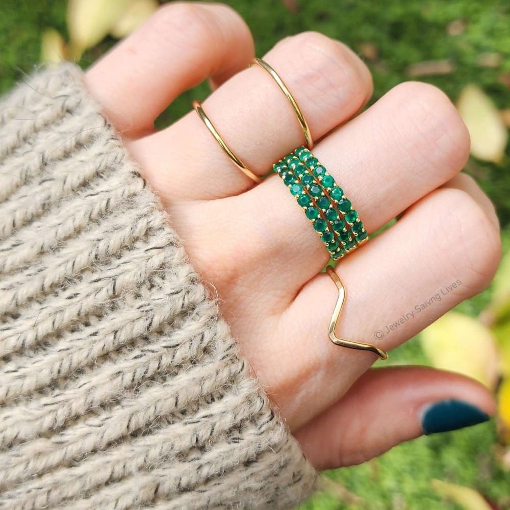 Gold and emerald half eternity band set worn on fingers with knit sleeve visible