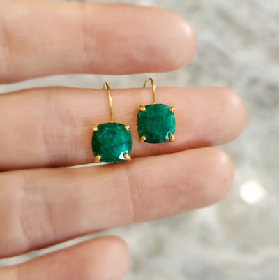 Gold earrings featuring round emerald green gemstones.