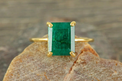 Gold ring featuring an emerald-cut emerald gemstone in a prong setting.