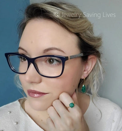 A person wearing navy blue rectangular glasses and emerald green jewelry.