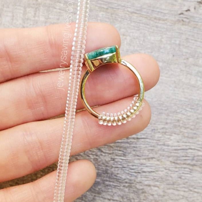 Gold ring with emerald stone and pearl accents beside a Plastic Ring Sizer