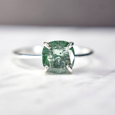 Silver ring with cushion-cut green emerald in prong setting, featuring Glowing Teal Diamond