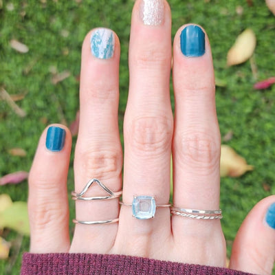 Hand with blue nail polish showcasing The Asher Natural Aquamarine ring with silver accents