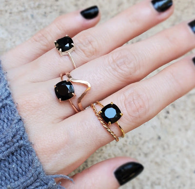 Three gold rings with black gemstones worn on fingers with black nail polish.